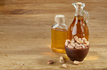 Aromatic oil in a glass jar and bottle with pistachios in bowl on wooden table, close-up.