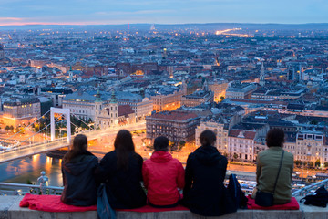 Group of sitting people overlooks Budapest city from top viewing point on Gellert hill