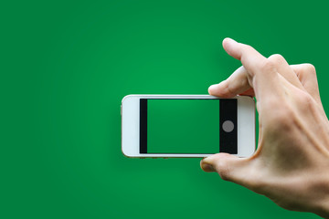 Hand holding mobile smartphone with blank screen horizontally on green background