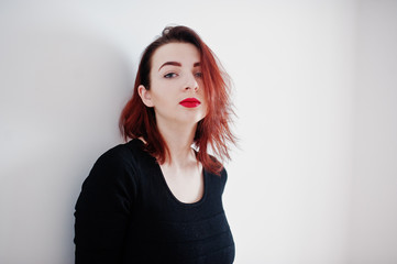 Naklejka premium Red haired girl on black dress tunic against white wall at empty room.