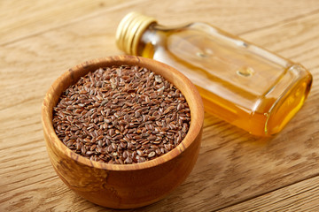 Flax seeds in bowl and flaxseed oil in glass bottle on wooden background, top view, close-up, selective focus
