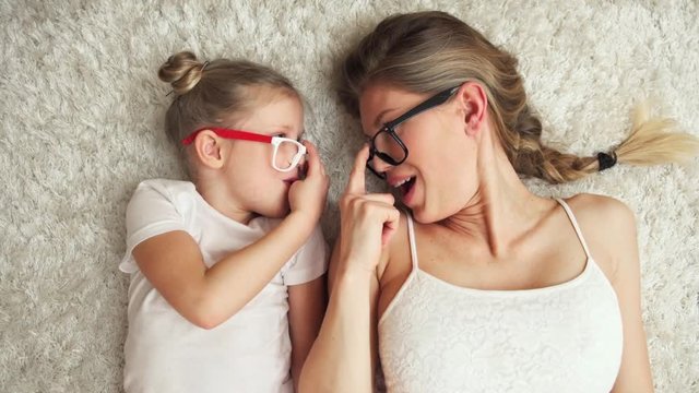 Funny footage of young woman with little daughter lying on the floor looking at each other in eyeglasses. 