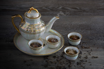 Chinese teapot set with cup which has hot tea and smoke in tray and dry tea leaf all on the plank