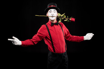 mime holding red rose in mouth and standing with open arms isolated on black
