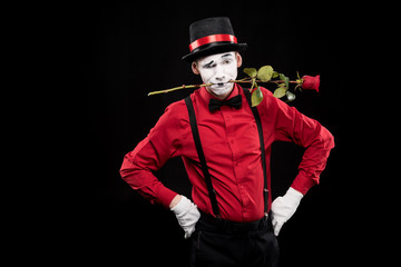 mime grimacing and holding red rose in mouth isolated on black
