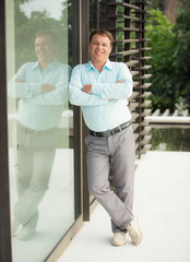 Smiling man stands leaning on a glass wall.