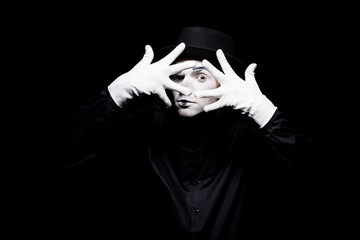 mime looking at camera through spread fingers isolated on black