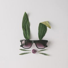 Bunny rabbit face made of natural green leaves with sunglasses on bright background. Easter minimal concept. Flat lay.