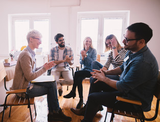 Group of excited and confident young people sitting in a row in the waiting room with a folder in hand before an interview with the entrepreneur and sharing personal details.