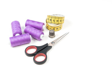 Sewing accessories and tools, orchid purple sewing threads, yellow measuring tape with black numbers, small scissors and metal thimble on a white background