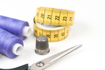 Sewing accessories and tools, medium purple sewing threads, yellow measuring tape with black numbers, scissors and metal thimble on a white background