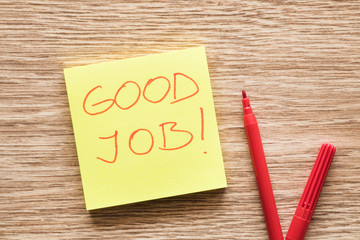 Inscription good job on the sticky note with red color pen on the office wooden desk. Praise from...