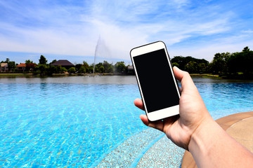 Hand hold Modern smartphone with blank screen at outdoor swimming pool and lake with beautiful sky. Copy space.