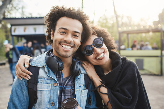 Two happy african-american travellers with afro hairstyle hugging and looking at camera, making photo while walking in park, expressing positive emotions. Friendship and relationship concept.