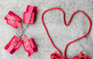 Red handcuffs and a rope for binding lined in the shape of the heart.