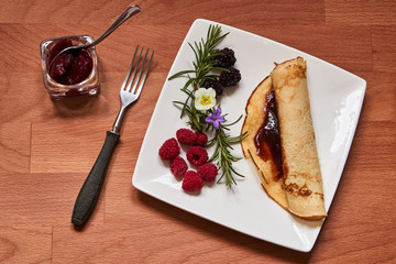 Plate with pancake and fruit on a wooden table top.