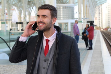 Joyful businessman calling by phone from train station