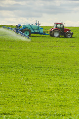 Tractor spraying pesticides on field with sprayer at spring