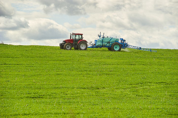 Fototapeta premium Tractor spraying pesticides on field with sprayer at spring
