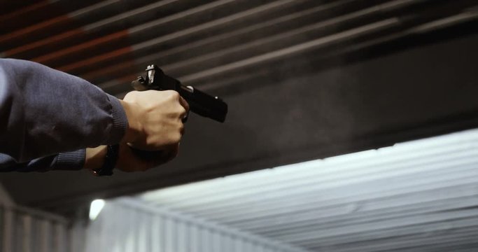 shooting targets in a range. A closeup of a pistol in his hand. one can see the fire from the barrel.