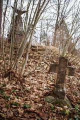 Old tombstone cross of the First World War overgrown with moss and old leaves in the autumn forest