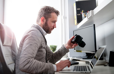 Fototapeta premium Photographer in home office working with laptop and looking at camera