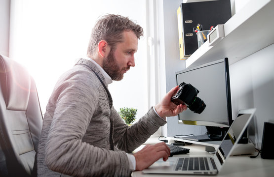 Photographer in home office working with laptop and looking at camera