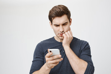 Indoor portrait of cute adult european man, expressing concern and worry while reading message in...