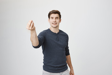 Indoor shot of serious looking guy giving speech, showing italian gesture with raised hand, standing over gray background. Actor performing play in front of audience in theatre