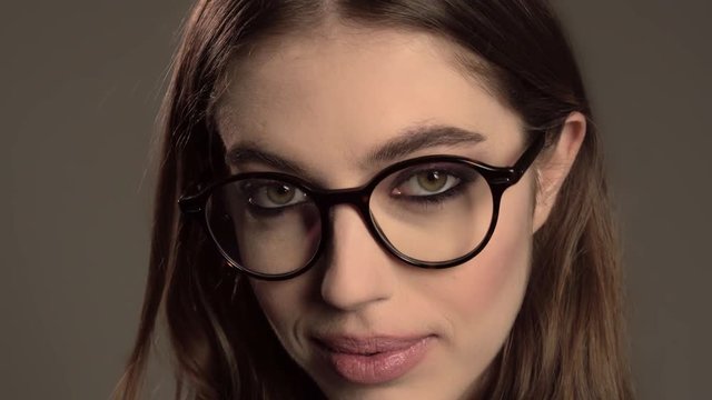 Indoor portrait of young good-looking girl in round glasses on gray background
