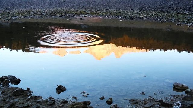 Stone falls into calm in Carezza lake water