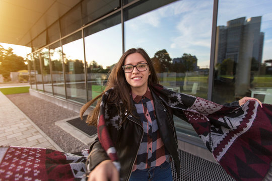 Young smiling female student near modern architecture in autumn sunset

