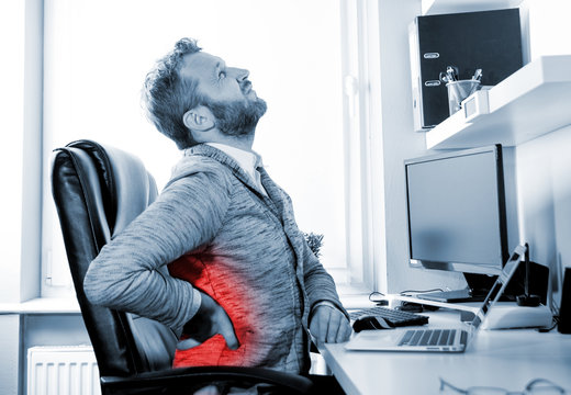 Man in office suffering from back pain, red dot around painful area