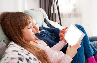 Happy children on sofa at home playing with digital tablet together
