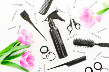 Hairdresser tools - spray, scissors, combs, barrette and tulips flowers on white background. Beauty concept. Flat lay, top view