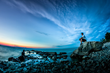 Beautiful landscape with sunset over the lake and a young man sitting on a rock, Iancina, Razelm Lake, Romania