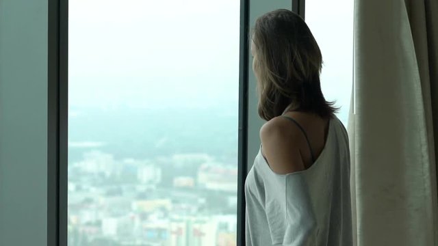 Young woman unveil curtain from window and admire view 
