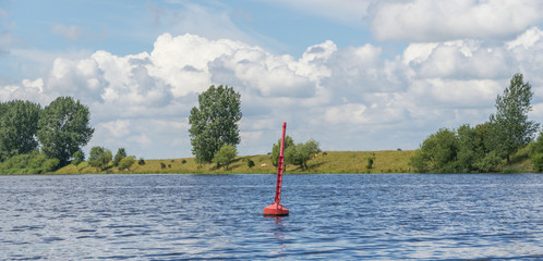 Rote Fahrwassertonne auf einem Fluss mit Ufer im Sommer