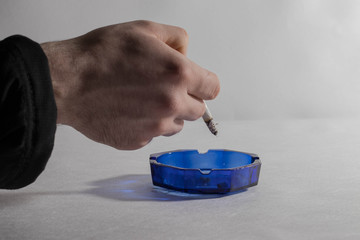 A female hand shake a cigarette in an ashtray on a gray background.