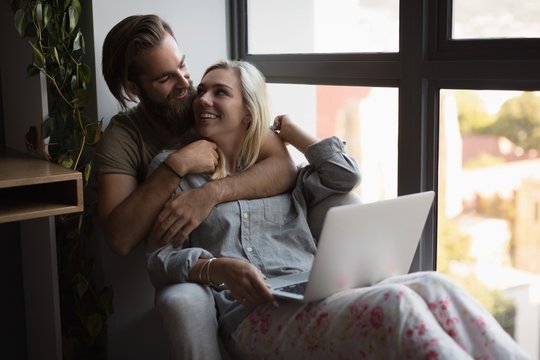 Couple embracing each other while using laptop
