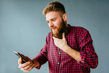 Emotional portrait of beard hipster man screaming while looking on his mobile phone over gray...
