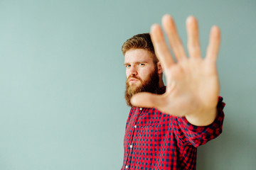 Handsome serious red head beard man making stop sign over turquoise background.