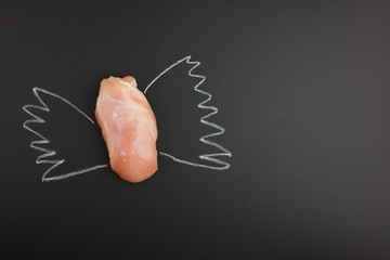 Raw chicken fillet with chalk drawn wings on a black background