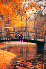 Two little girls sitting on wooden bridge and pretend fishing; autumn background