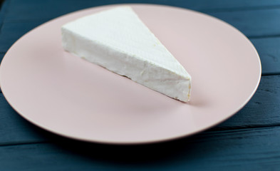 A piece of brie cheese on a plate on a wooden dark blue background.