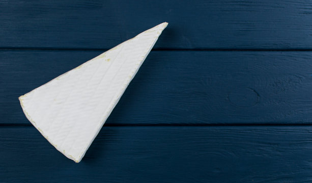 A piece of brie cheese on a wooden dark blue background.