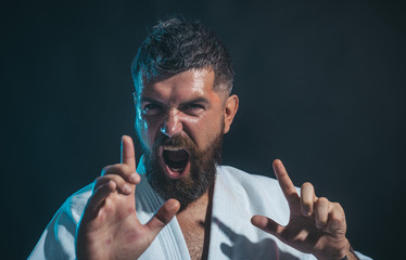 Portrait of screaming karate master instructor. Karate man in action. Karate fighter showing kick by hand. Karate man in white kimono on black background.