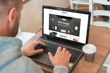 Web designer designs a modern flat website on a laptop. Coffee beside.