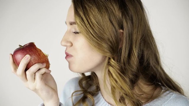 Seductive fair haired woman in gray biting a red juicy apple and chewing it. She is looking at you and licking her lips. Locked down real time close up shot