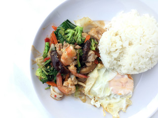 Vegetable stir-fry dish with Thai healthy food stir-fried broccoli, mushroom, carrot, hearb, squid and shrimp with rice and fried egg in white plate on white background.  Thai style fast food can orde